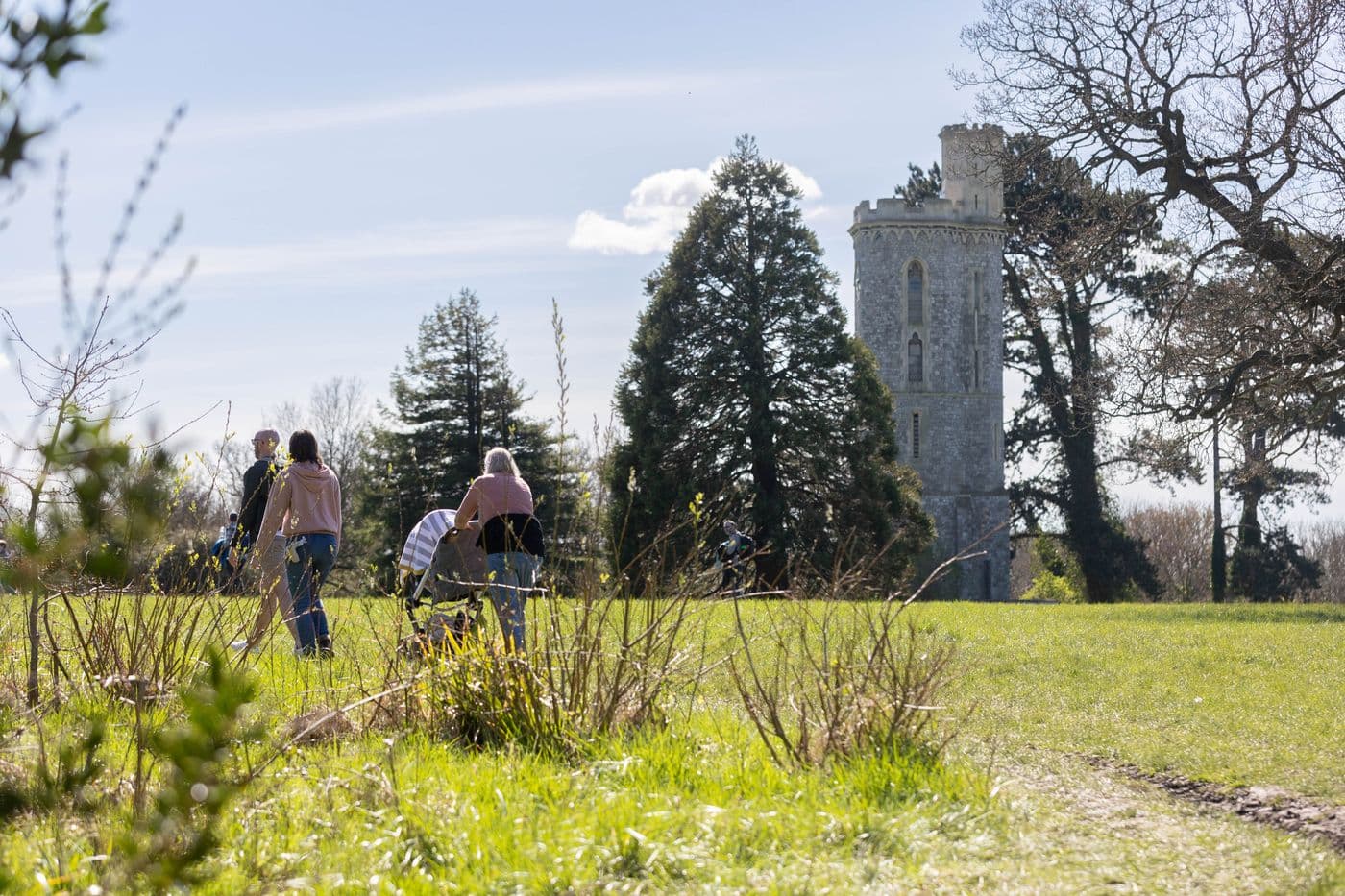 A group of people with a push chair are walking in tower meadow. The tower is seen in the background.