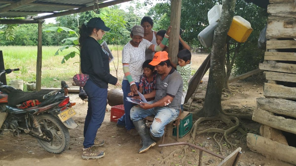 A lady working talking to a local community in Colombia. The villagers are looking at pictures in their back garden